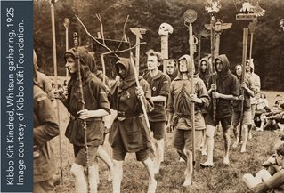 Sepia tinted image of a march in rural setting with males dressed in woodland clothing and carrying rustic banners and lances. Kibbo Kift from Bella Pollen research.