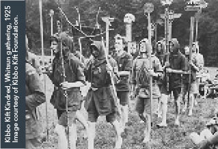 Black and white image of a parade of young men and boys carrying carved totems and wearing rustic tunics. Title reads, Kibbo Kift Kindred, Witsun gathering 1925. Courtesy of Kibbo Kift Foundation.