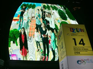Digital artists Paul Sermon and Charlotte Gould installed the thematic work People's Screen in Guangzhou, China. Image shows large screen with multiple figures and a banner with the event title.