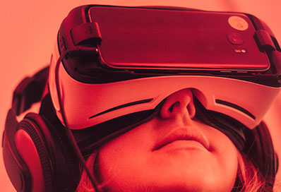 A red toned image of a woman wearing a virtual reality headset, working with digital research projects at the University of Brighton.