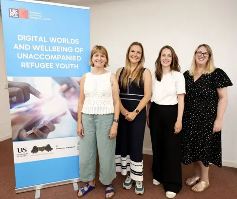 Four members of the Digital Worlds team standing next to a banner