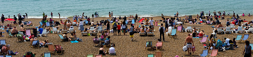 Banner image representing human geography through a photograph of Brighton beach in summer, crowded with striped deckchairs and sunbathers.