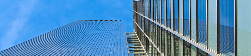 Dramatic low angle photograph looking up at glass and steel skyscrapers against blue sky.