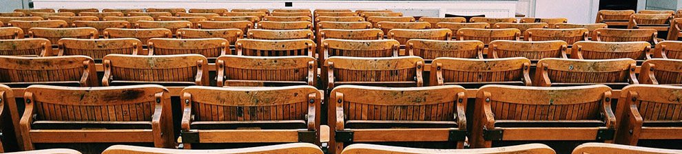 Image illustrating education policy and practice research shows rows of worn wooden chairs with book holders on the backs.