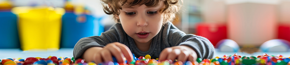 Young boy concentrating on sorting coloured beads. A representation of occupational therapy research.