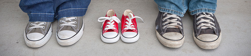 Illustrating podiatry research, two pairs of large trainers in grey with a small pair of trainers in red between them.