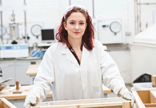 Student researcher in white coat works within a workshop research environment.