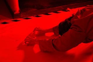 Ola Teper, PhD art candidate. Still from performance of Cameron's Thumb (2024). Red-lit figure bent head and scratching floor.