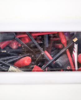Perspex viewing strip in wall shows black and red handled toothbrushes in a jumbled heap. Part of the wall insulation in the Brighton Waste House