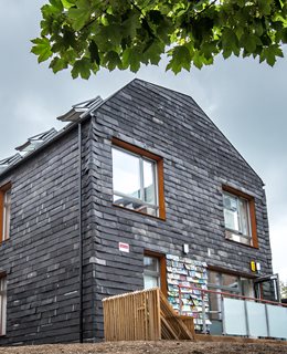 Waste House May 2014. Two storey building with three windows and a door on main facade. Clad in grey rubber tiles.