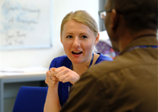 Mentoring one-to-one, photograph viewed over mentor's shoulder to see engaged face of mentee. Whiteboards in background.