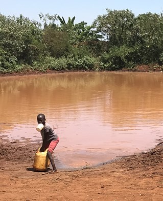Young Kenyan child collects water at a brown pool. Water contamination research from the University of Brighton.