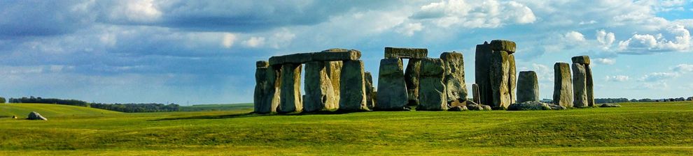 Brightly lit distant view of Stonehenge under blue sky with tourists watching. Courtesy Darius Chandra and Pixabay.