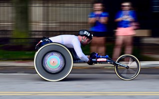 Panned photograph of wheelchair road racing athlete with blurring in background and large rear wheels. Image courtesy Joseph Two.