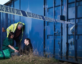 Paramedic and medical professionals attend an unconscious person with a Police line do not cross tape running across the foreground