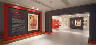 The Wolfsonian Florida International University. Entrance to graphic design exhibition 'Julius Klinger: Posters for a Modern Age'. Large plinth and red and grey decor in wide gallery space.