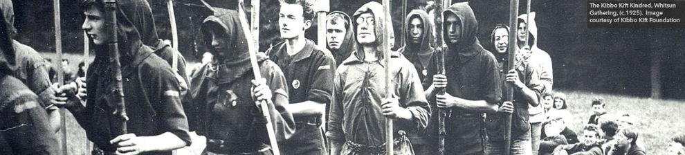 Grainy black and white photograph of a ceremonial procession. Men and boys are dressed in jerkins and hoods and carry poles with carved designs. Inset plate reads Whistun Gathering of the Kibbo Kift Kindred circa 1925. Image courtesy of the Kibbo Kift Fou