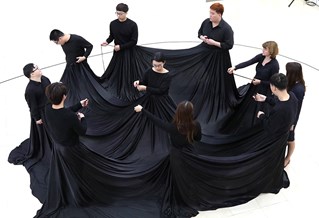 Performance at the Korean Disability Arts and Culture. Ten artist participants stand in a circle with a large black fabric prop around and between them.