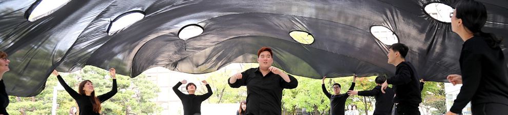 Performance directed by Alice Fox at Korean Disability Arts Festival. Vast black fabric square billows into the air above a group of artist participants, each of whom now moves inwards, under it.