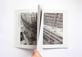 Hand holds a book of photographic images to show Pages 28 and 51 and the black and white photograph of a destroyed high-rise building that goes through the fold. Photographs collected and analysed by Xavier Ribas and Louise Purbrick in Traces of Nitrate. 