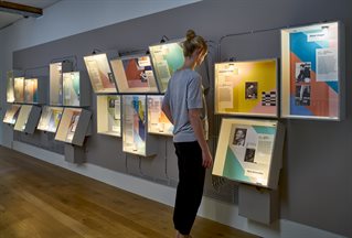 Wall display of images related to design with visitor. Photograph by Leon Chew from the exhibition Designs on Britain. 0019