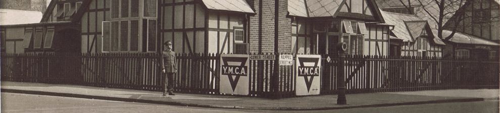 Sepia photograph across a road towards a single-storey mock-Tudor building with tall chimney stack. A man in World War One soldiers' uniform stands in front. The former YMCA building known as the Shakespeare Hut.