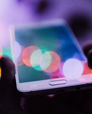 Sunflare on mobile phone held up between fingers. Image by Rodion Kutsaev via Unsplash