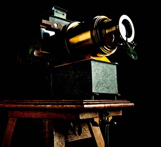 An antique slide projector photographed artistically lit against black background. The model is The Verlux used by the Church Army Lantern Department, circa 1918.