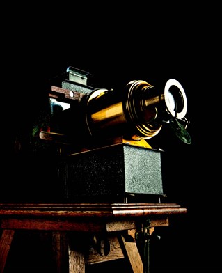 An antique slide projector photographed artistically lit against black background. The model is The Verlux used by the Church Army Lantern Department, circa 1918.
