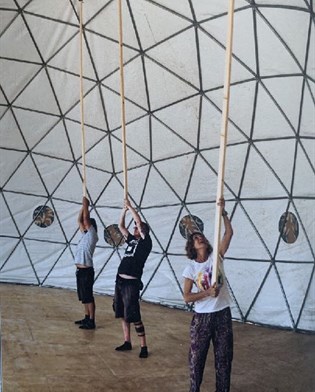 Co-workers on refugee displacement projects use large poles to finish creating a fabric and wireframe dome. Research by Robert Mull on architecture of displaced communities.
