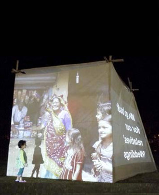 A small child stands against a built cube of fabric on which images and messages are projected. Paul Sermon 3x4 Labs art work exploring Future Cities