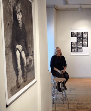 Curator and researcher Julia Winckler seated at her Exhibition Les Enfants de la Cite, black and white framed photographs and contact sheets on white walls.