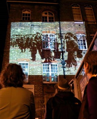 Spectators look up to a projection onto a building. Julia Winckler's work reactivating archive photography of areas of Brighton.