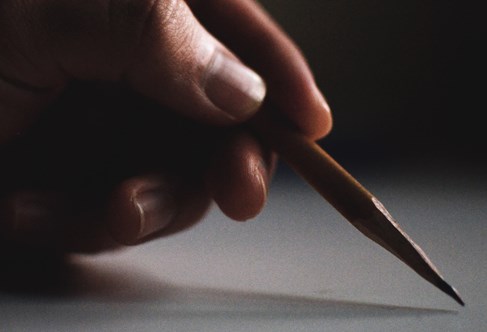 Dramatically lit image of hand holding a pencil before mark-making illustrating art and design practice in a research context. Courtesy Samuel Rios and Unsplash.