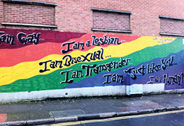 Rainbow painted wall with the words 'I am Gay/I am Lesbian/I am Bisexual/I am Transgender graffitied on it.
