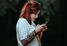 Girl with a tattooed arm looking at her phone.