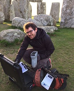 Researcher with Stonehenge stones in the background unpacks geological research observation tools.