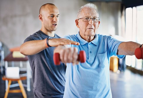 Older person being guided by a coach as they lift hand weights