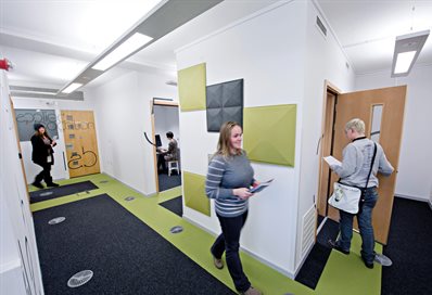 A photograph of a designed university room showing three women walking through in sequence on a marked pathway.