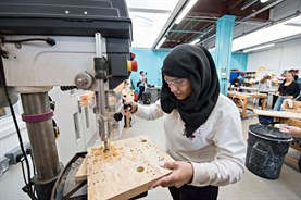 Female student using a machine cutting shapes in wood