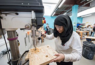 Female student using a machine cutting shapes in wood