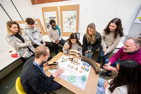 Students crowded round a table with spatial design model structure