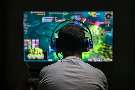 gamer viewed from behind, their head with earphones silhouetted in the screen