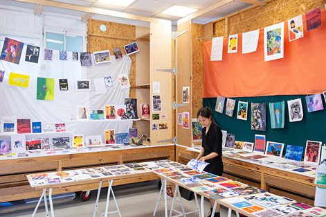 female student prepares artwork for graduate show, artwork hangs on string and is laid out on a table