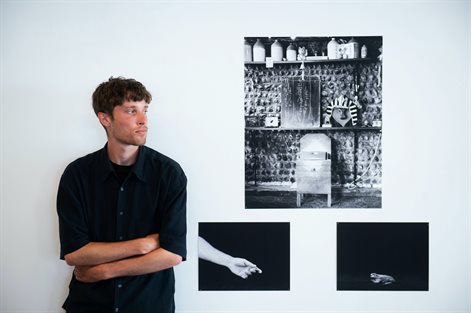 student dressed in black leans on wall beside three photos on wall