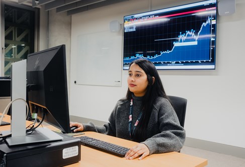 Student working at a computer in the Bloomberg Suite with a graph of data shown behind her