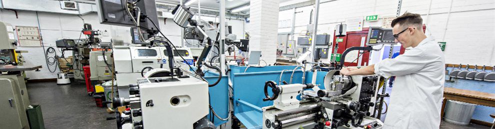 A student in a white coat using the lathe in the engineering lab