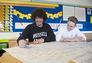 Two students writing on large pieces of paper from a flip chart