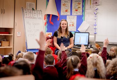 Children in a classroom with their hands up to answer a question