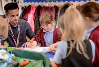 male trainee teacher with group of primary children